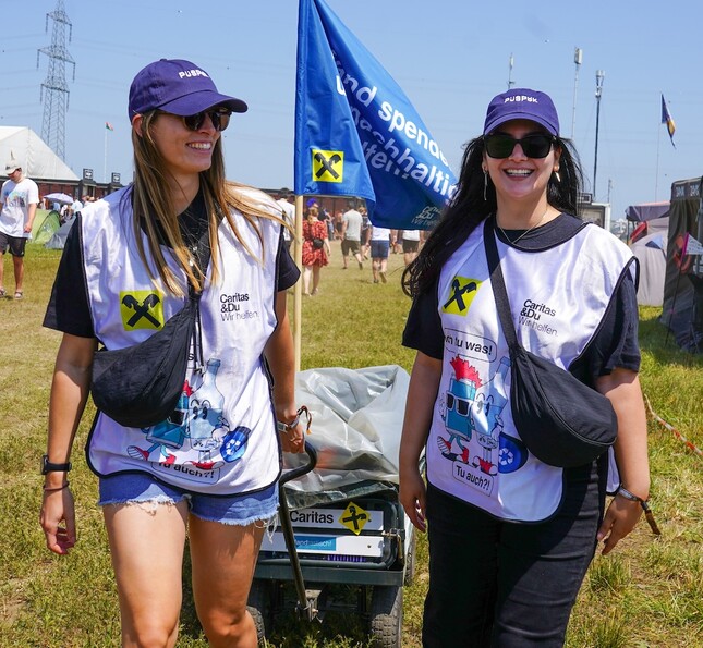 Zwei Frauen mit Caritas Weste ziehen einen Wagen voller Pfand. 