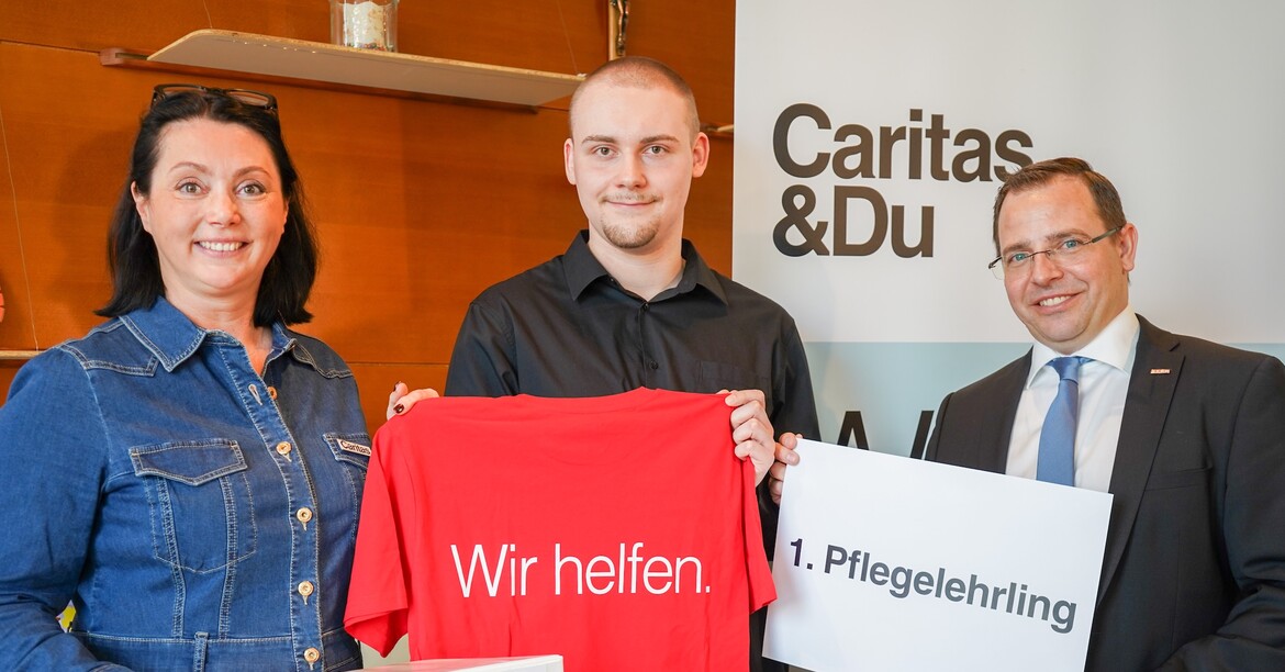 Pressefoto des ersten Pflegelehrlings mit zwei Caritas Mitarbeiter*innen.