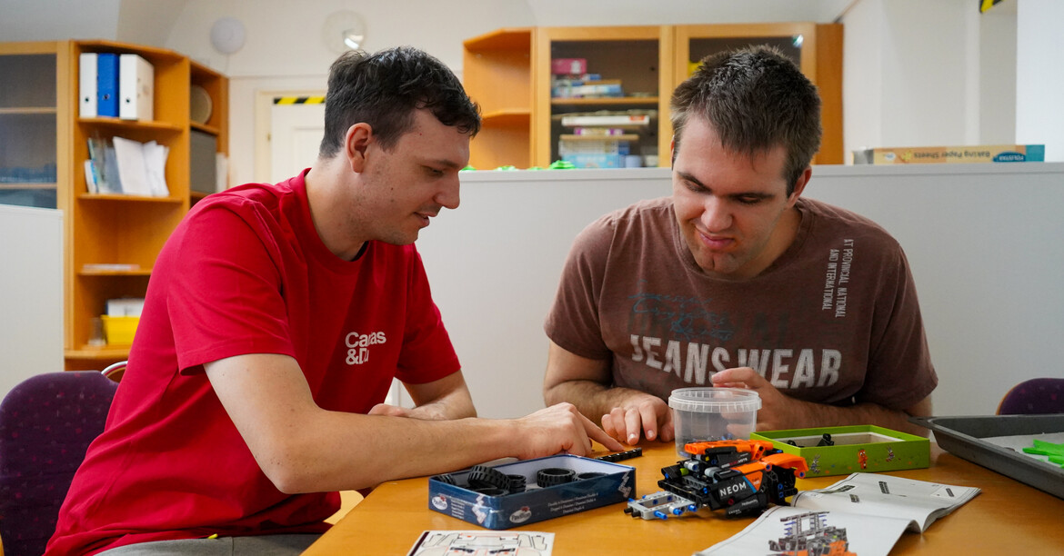 Zwei Männern blicken konzentriert und bauen ein kleines Spielzeugauto.