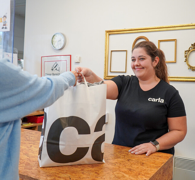 Eine Verkäuferin reicht einer Kundin ihre gekaufte Einkaufstasche.