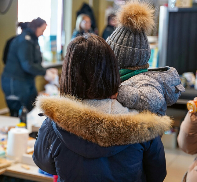 Eine Frau steht mit ihrem Kind im Arm mit dem Rücken zur Kamera. 