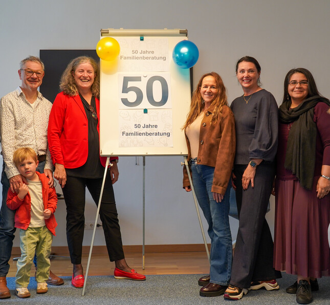 Berater*innen stehen vor einem Schild auf dem "50 Jahre Familienberatung" steht.