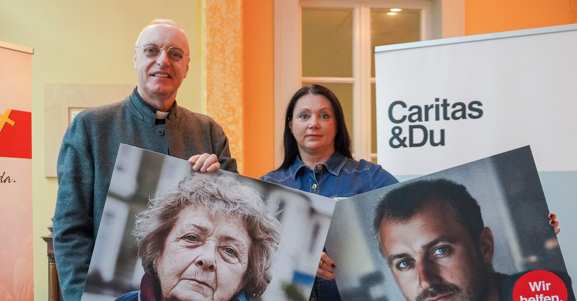 Caritas Direktorin und ein Mann stehen vor zwei Roll-ups mit Bildern in der Hand. 
