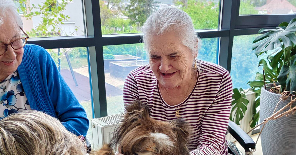 Eine Bewohnerin lacht vor Freude während sie einen Therapiehund streichelt.