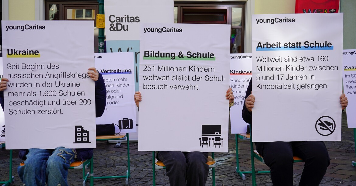 Schülerinnen und Schüler halten Schilder mit Fakten und Zahlen über Bildung und Armut weltweit.