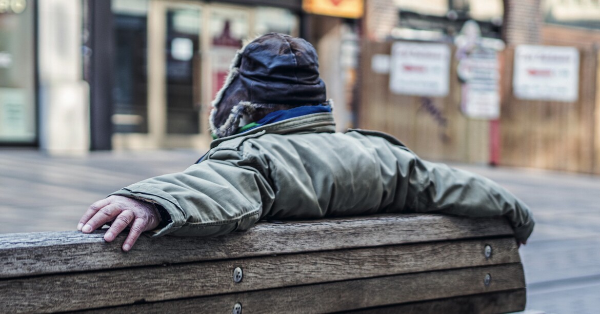 Ein Mann sitzt auf einer Bank mit Winterjacke und Haube. 