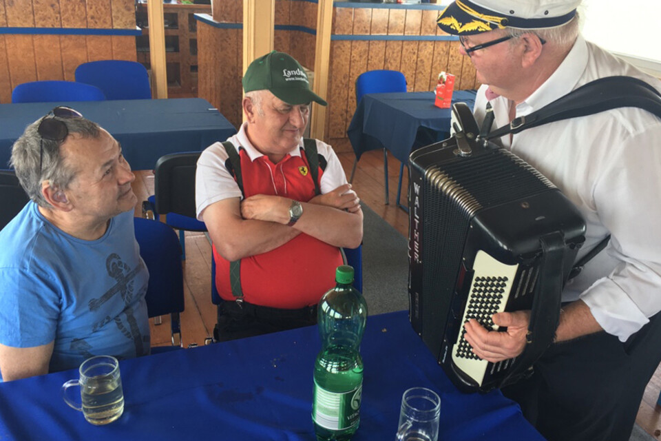 Zwei Bewohner vom Caritas Haus St. Stephan mit einem Zieharmonikaspieler am Schiff