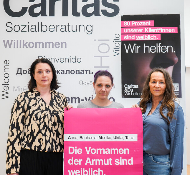 Drei Frauen halten ein rosa Plakat in den Händen.  