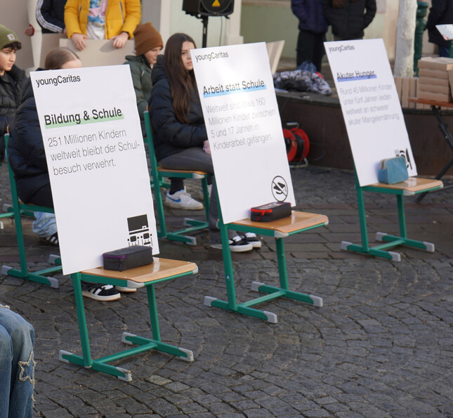 Auf Stühlen stehen Schilder mit Fakten und Zahlen über Bildung und Armut weltweit.