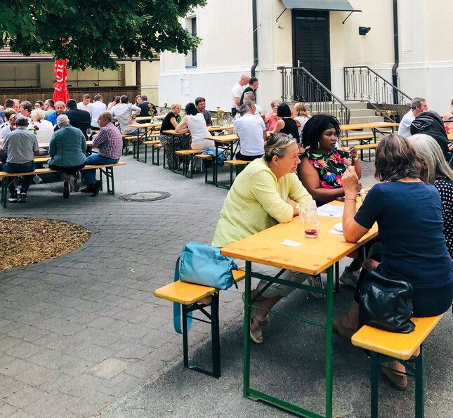 Gäste sitzen auf Heurigenbänken im Pfarrzentrum und essen.