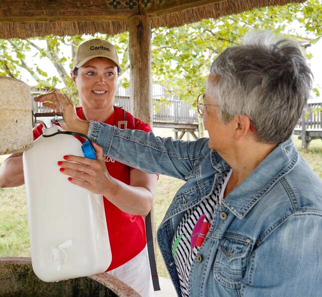 Caritas Direktorin beim auffüllen von einem Wasserkanister zusammen mit einer Frau. 