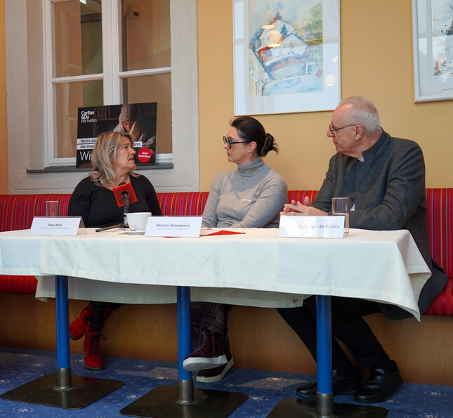 Drei Person sitzen bei einer Pressekonferenz vor Mikrofonen.